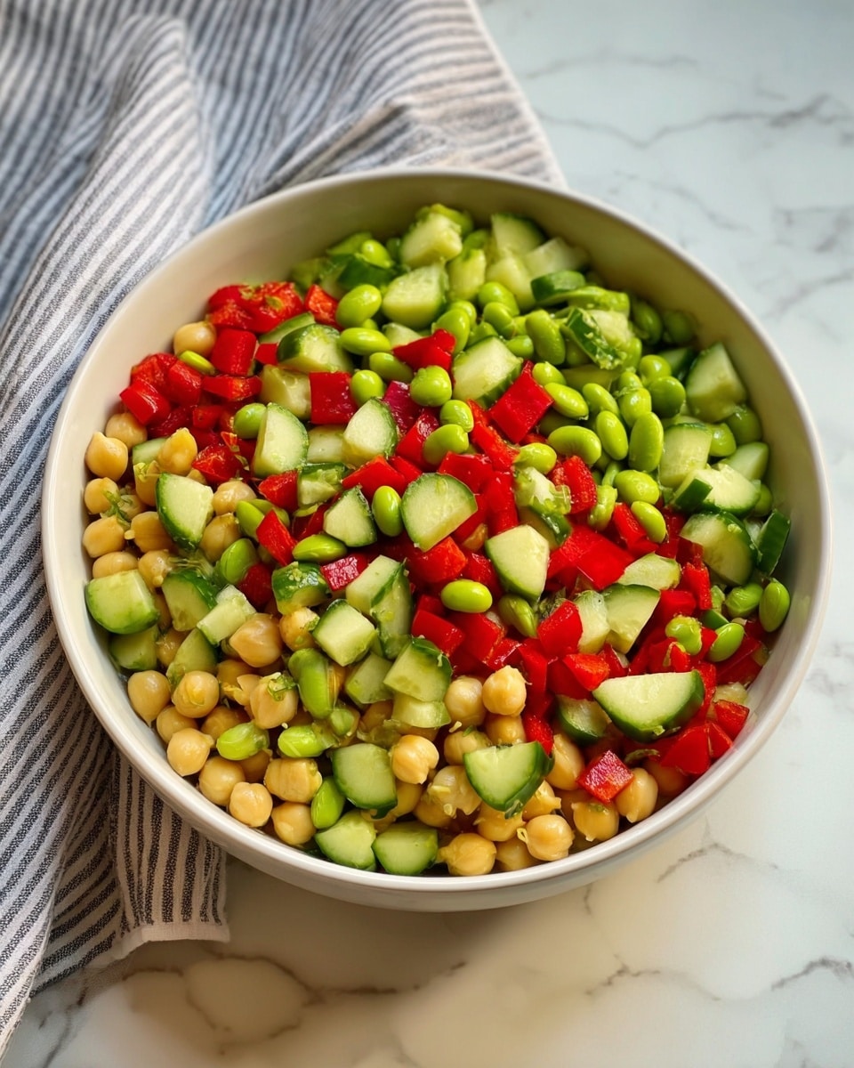 Three clear rectangular glass containers are arranged on a wooden cutting board over a white marbled surface with a blue-striped cloth nearby. Each container has two distinct layers: one side filled with a mix of chopped green cucumbers, red bell peppers, green beans, and beige chickpeas, creating a colorful, fresh vegetable layer with varied textures; the other side holds a light beige shredded chicken or a creamy white cottage cheese, neatly separated from the vegetables. The light from above makes the colors bright and inviting. Photo taken with an iphone --ar 4:5 --v 7