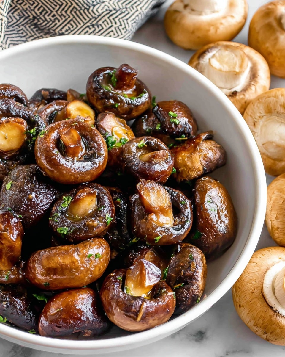 A white bowl filled with shiny cooked mushrooms showing deep brown colors with some blackened edges, garnished with small bits of green herbs, each mushroom sliced into halves or quarters revealing soft textured insides. Around the bowl, fresh whole mushrooms with light to medium brown caps and white stems sit on a white marbled surface, providing a fresh contrast. The mushrooms in the bowl have a glossy, slightly oily appearance, making them look well-seasoned and juicy. Photo taken with an iphone --ar 4:5 --v 7