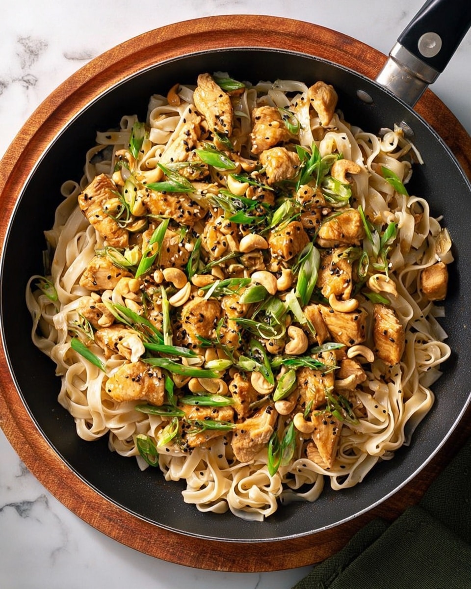 A skillet filled with a dish showing three main layers: at the bottom, there are wide, flat rice noodles that are pale beige and slightly shiny; above, scattered chunks of light brown cooked chicken pieces are mixed evenly; the top layer has bright green sliced spring onions and golden cashew nuts spread throughout, all sprinkled with small black sesame seeds. The skillet is placed on a wooden board, and the background has a white marbled texture. Photo taken with an iphone --ar 4:5 --v 7