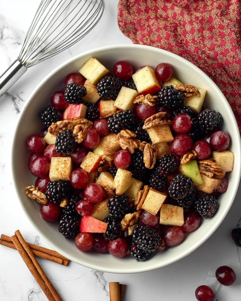 A close-up view of a white bowl filled with a mixed fruit salad showing three main layers: the bottom layer with dark purple and black blackberries, the middle layer with red grapes and cubed pieces of light yellow and reddish apple coated lightly in cinnamon powder, and the top layer featuring scattered light brown pecans and small crunchy walnut pieces. The bowl sits on a white marbled texture surface with two sticks of cinnamon placed diagonally near it, and a silver whisk and red cloth are visible in the background. The fruits glisten under soft lighting, highlighting their fresh and juicy textures. photo taken with an iphone --ar 4:5 --v 7