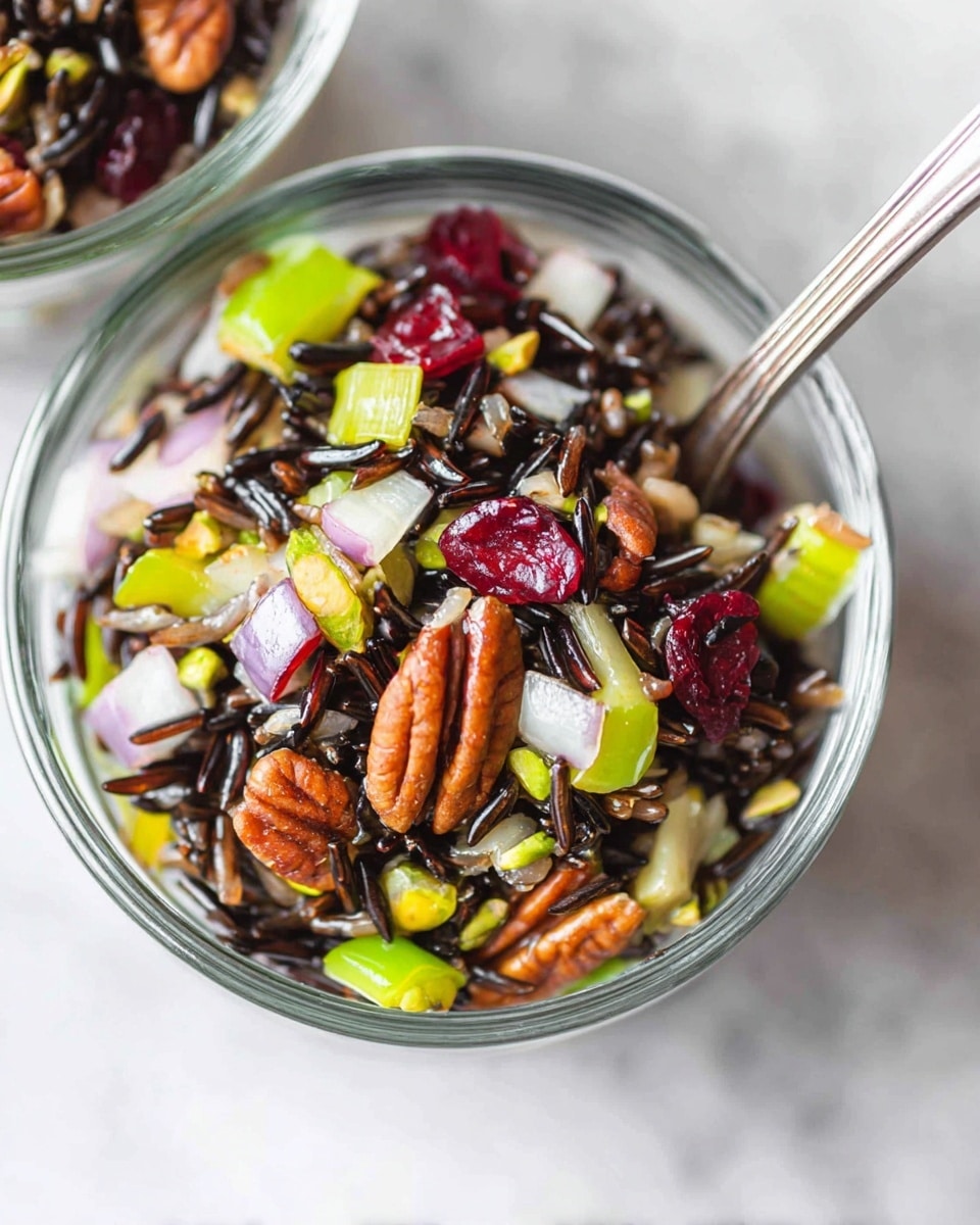 A clear glass jar filled with a layered wild rice salad. At the bottom are dark, long wild rice grains mixed with small pieces of green celery and red onion. Above this, there are bright orange chunks of sweet potatoes, dried dark red cranberries, and some nuts. The salad shows different colors and textures, all mixed together in the jar. The background is a soft white marbled texture with part of a light brown and white cloth visible. photo taken with an iphone --ar 4:5 --v 7