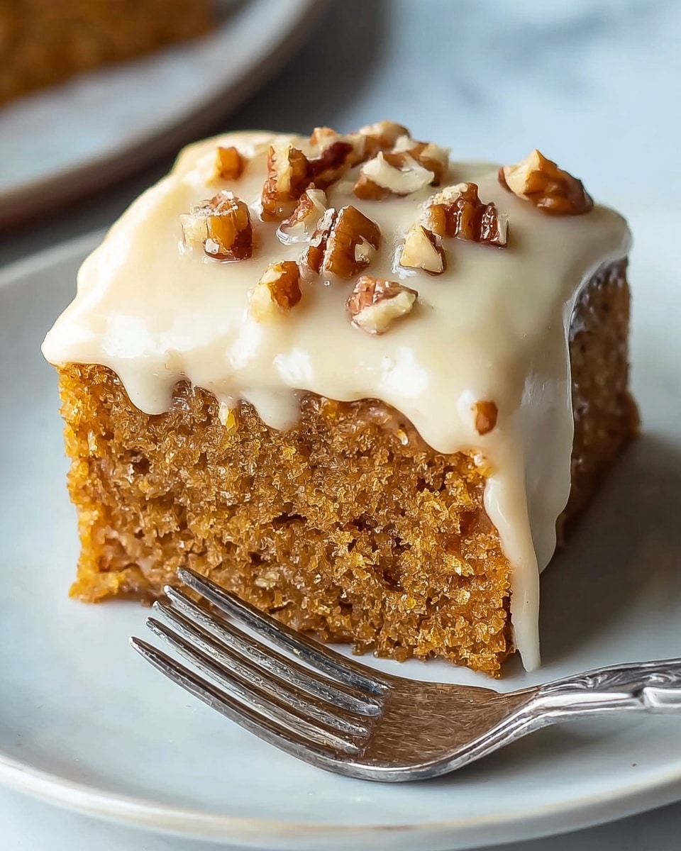 A single square piece of moist, light brown cake sits on a white plate with a silver fork beside it. The cake has a soft, crumbly texture with visible tiny air pockets. It is covered with a thick layer of smooth, creamy beige frosting that drips slightly down the sides. On top of the frosting, there are chopped pecan pieces scattered, giving a crunchy contrast. The plate is placed on a white marbled surface, and the background is softly blurred. photo taken with an iphone --ar 4:5 --v 7