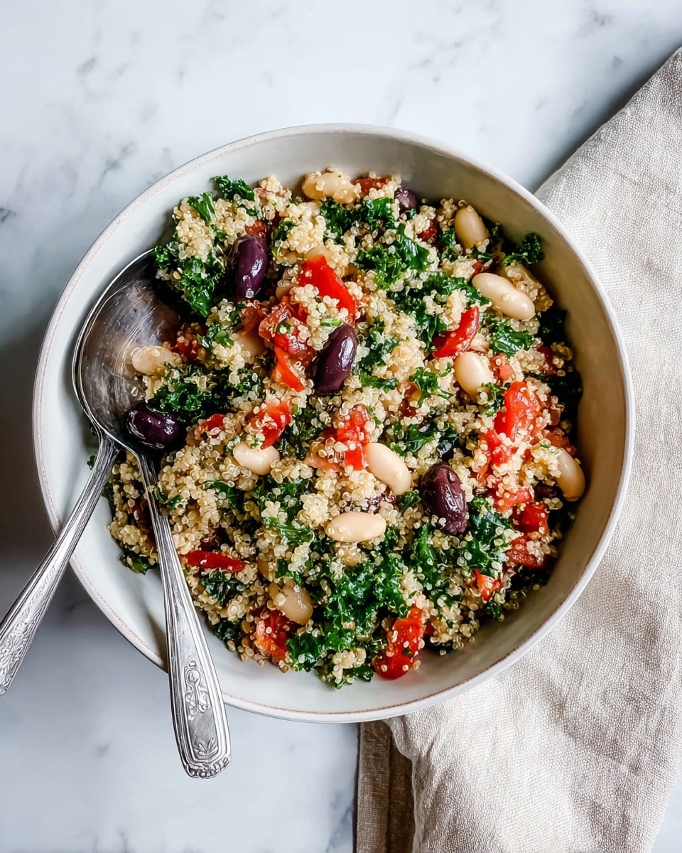 A round deep white bowl filled with a mixed quinoa salad showing about four layers: the bottom layer is light beige fluffy quinoa grains, mixed with kidney beans that are dark purple and smooth, white beans which look plump, diced red tomatoes with a juicy texture, and chopped bright green kale leaves scattered evenly throughout. Two silver forks rest inside the bowl on the lower right side, slightly embedded in the salad. The bowl sits on a white marbled surface next to a soft beige cloth napkin on the right. The photo taken with an iphone --ar 4:5 --v 7