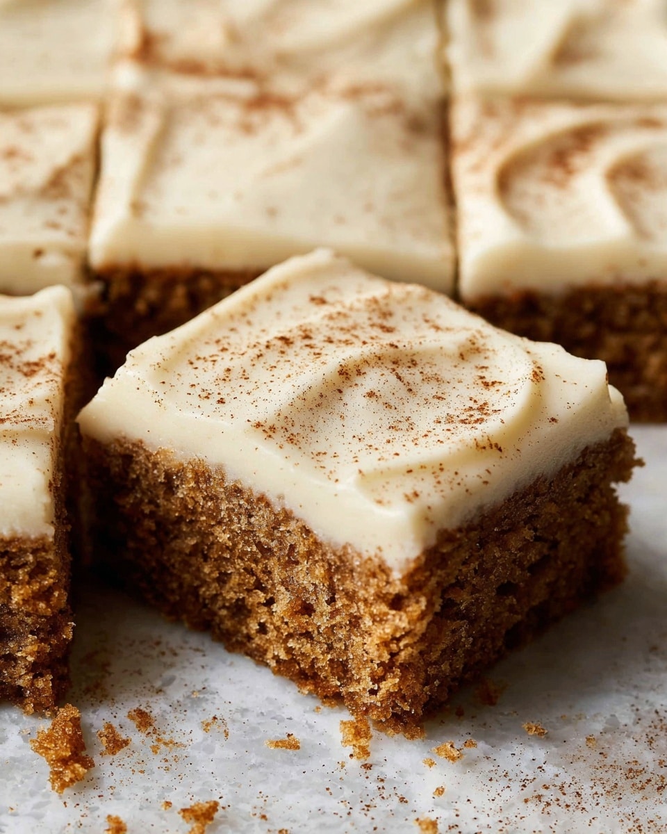 A square piece of moist brown cake with a rough, crumbly texture sits on a white plate with a slightly wavy edge. On top of the cake is a thick, smooth layer of light beige frosting spread evenly with some soft swirls and tiny specks of spice. A silver fork holds a bite-sized piece of the cake, lifting it slightly from the corner. The background is softly blurred with a white marbled texture surface underneath the plate. Photo taken with an iphone --ar 4:5 --v 7