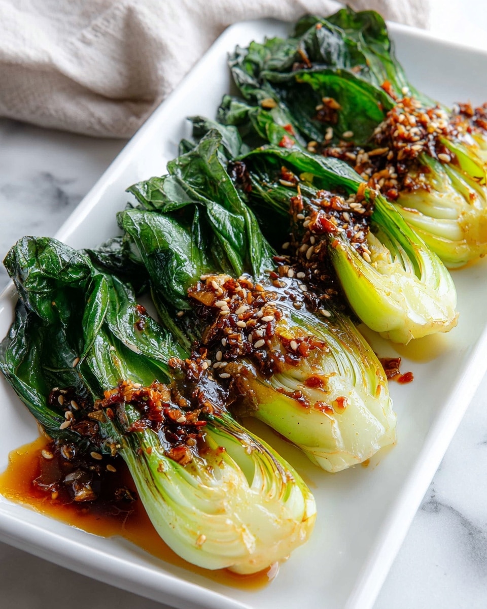 A white rectangular plate holds four pieces of cooked bok choy neatly lined up side by side, each bok choy having two main layers: the top pale green and slightly translucent stalks with a light glaze, and the bottom dark green leafy parts, slightly wilted. The bok choy is topped with small bits of dark brown garlic and sesame seeds scattered evenly, coated in a shiny, rich brown sauce that pools slightly around the base of the vegetables. The plate rests on a white marbled surface with a soft, light-gray cloth casually draped nearby. Photo taken with an iphone --ar 4:5 --v 7