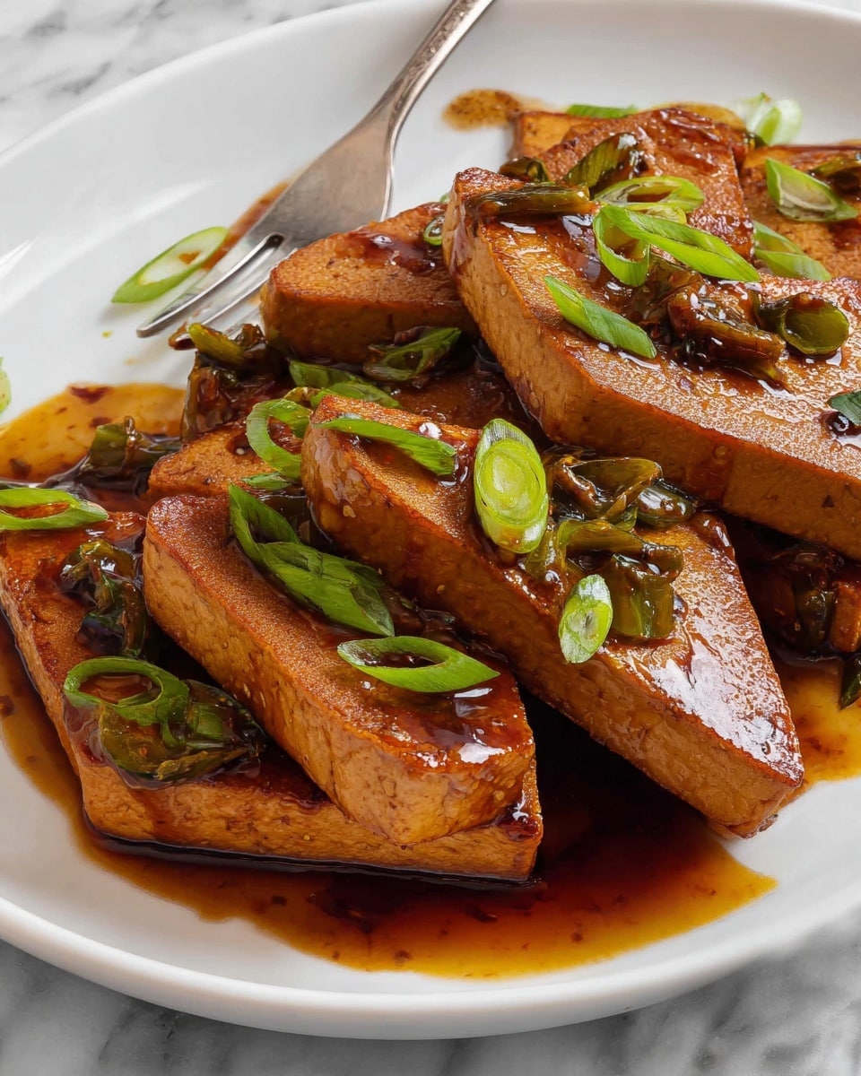 The image shows a white rectangular baking dish filled with a dark brown sauce that has chopped green onions and small pieces of garlic floating in it. Inside the sauce, there are several large, thin, triangular slices of tofu, pale beige in color with a slightly rough texture and some specks of seasoning on top. The triangles are arranged in a scattered manner, partially submerged in the sauce, giving a moist and flavorful look to the tofu. The dish rests on a white marbled textured surface. photo taken with an iphone --ar 4:5 --v 7