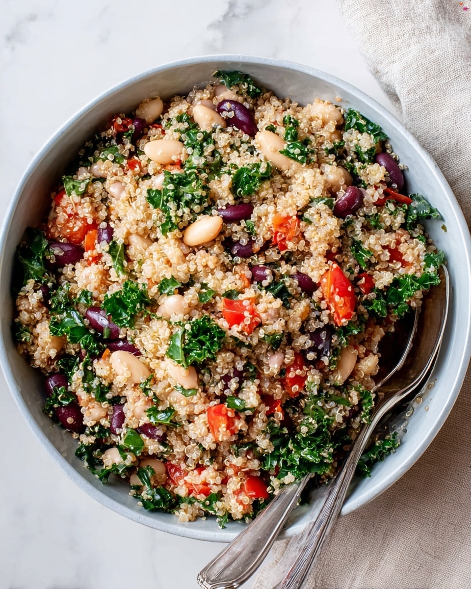 A deep white bowl filled with a mixed quinoa salad showing about five layers of ingredients: the base is light-colored quinoa grains with a fluffy texture, mixed through with bright red chopped tomato pieces spread evenly, leafy green kale pieces adding a fresh rough texture, white beans scattered throughout, and larger dark purple olives adding contrast. Two silver spoons rest inside the bowl on the left side. The bowl sits on a white marbled surface with a light beige cloth to the right side. photo taken with an iphone --ar 4:5 --v 7