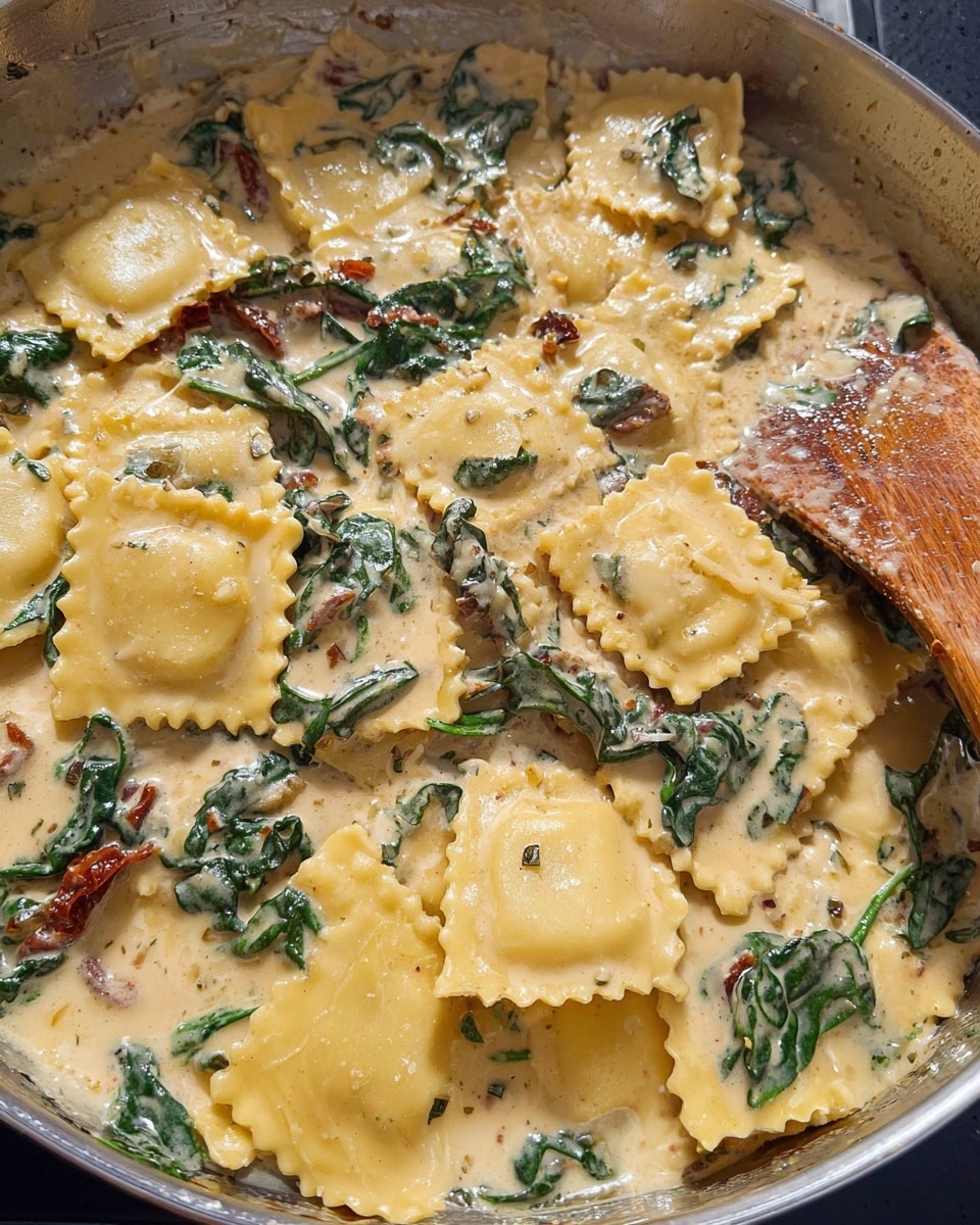 A white bowl filled with large square ravioli pasta coated in a creamy light brown sauce, layered with dark green wilted spinach leaves and pieces of sun-dried tomatoes scattered throughout; the sauce has visible black pepper specks, covering the pasta and vegetables evenly, creating a rich and textured look. The bowl is set on a blue and white cloth with a white marbled texture underneath. photo taken with an iphone --ar 4:5 --v 7
