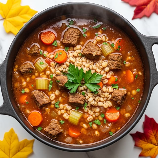 A close-up view of a dark brown cooking pot filled with a thick beef barley soup, showing a rich reddish-brown broth packed with several layers of ingredients: tender chunks of beef, small orange carrot pieces, translucent celery cubes, shiny barley grains, and small green herb sprinkles on top. The soup surface is glossy, with visible steam and some fresh parsley placed right in the middle as garnish. The pot sits on a white marbled surface with scattered yellow, orange, and red autumn leaves around it. Photo taken with an iphone --ar 4:5 --v 7