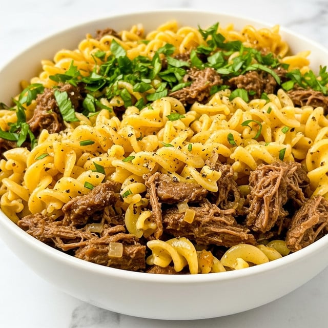 A close-up view of a white bowl filled with a pasta dish featuring two main layers: a base layer of soft, curly noodles in a light golden color mixed with tender chunks of shredded dark brown meat, and a top layer sprinkled with bright green chopped herbs, adding fresh contrast. The noodles appear glossy, coated with a thin oily sauce with specks of black pepper and small bits of herbs scattered throughout. The bowl sits on a white marbled surface. photo taken with an iphone --ar 4:5 --v 7