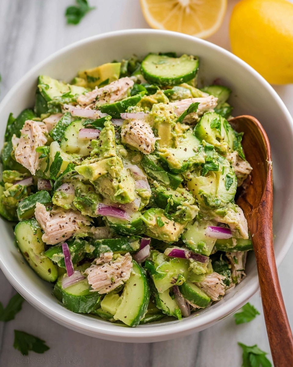 A white bowl is filled with four main layers neatly placed side by side: light beige shredded chicken seasoned with black pepper on the right, bright green chopped fresh cilantro in the middle, sliced pale green avocado with black pepper and olive oil at the bottom, thin slices of purple-red onion on the left, and quartered cucumber slices with their dark green skin at the top left. The bowl sits on a white marbled surface, with parts of two yellow lemons visible at the bottom right. Photo taken with an iphone --ar 4:5 --v 7
