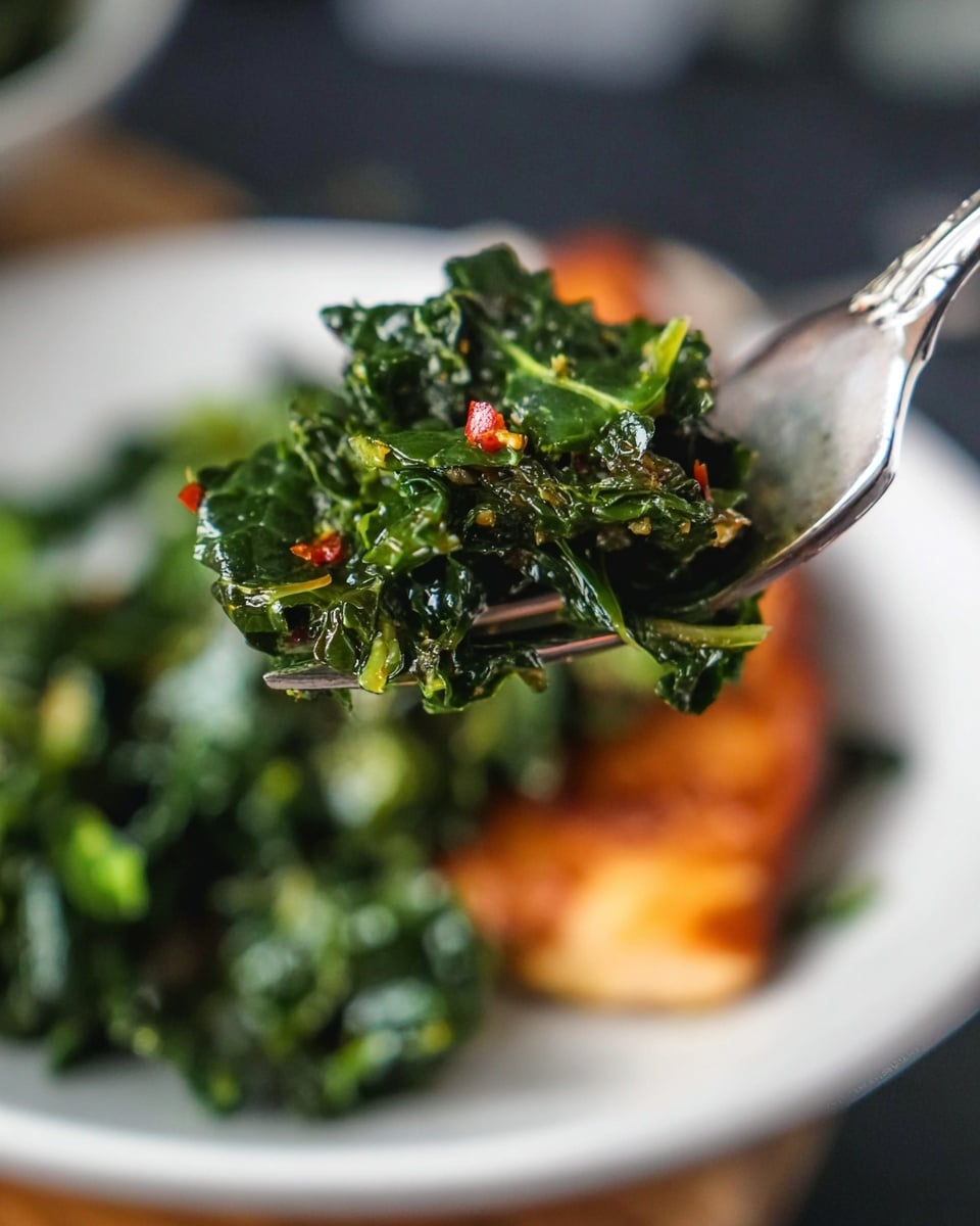 A white plate holds a piece of cooked salmon on the right side, with a crispy, browned surface showing a mix of orange and dark reddish tones, and a slightly charred edge. Next to it, on the left side, is a pile of cooked dark green kale with some bright green stems and small red chili flakes sprinkled on top, giving it a textured and fresh look. A silver fork rests on the plate behind the salmon. The plate sits on a white cloth over a dark wooden surface with a white marbled texture in the background. photo taken with an iphone --ar 4:5 --v 7
