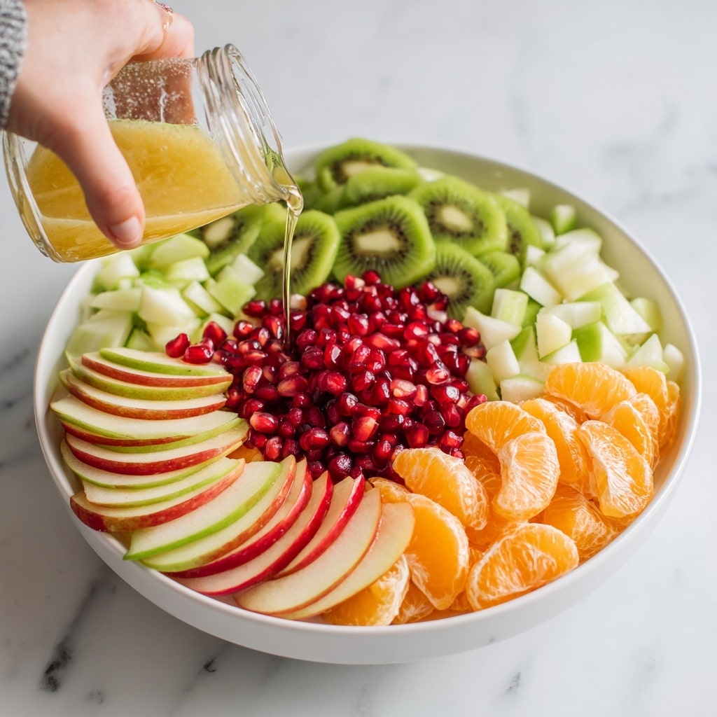A large white bowl filled with four layers of fresh fruit arranged in a circle: the bottom layer is green and red apple slices, the next layer is peeled and chopped green pear pieces, above that is sliced green kiwi with black seeds, followed by a layer of orange tangerine segments, and in the center, a pile of bright red pomegranate seeds. A woman's hand is pouring light yellow-orange dressing from a clear glass jar over the pomegranate seeds. The bowl sits on a white marbled surface. photo taken with an iphone --ar 4:5 --v 7