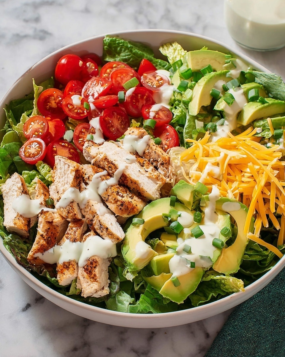 A white bowl filled with a fresh salad sits on a white marbled surface. The salad has three main layers: at the bottom, a base of green leafy lettuce; in the middle, bright red cherry tomatoes cut in half, thinly sliced yellow cheddar cheese, and light green avocado slices arranged neatly; on top, pieces of grilled chicken breast with visible seasoning. A thick white dressing is drizzled over the salad. To the side, there is a small yellow bowl with more creamy dressing, and two small green salt and pepper shakers next to a clear glass of water. Photo taken with an iphone --ar 4:5 --v 7