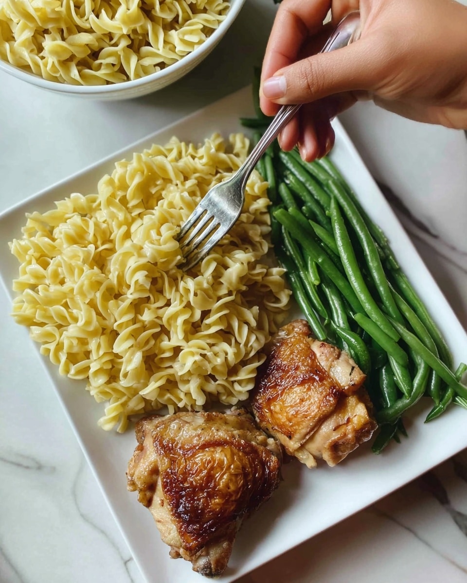 A white square bowl filled with creamy, cooked rotini pasta, coated in a smooth light yellow sauce with small bits of herbs and seasonings visible, giving texture and slight color variations; a woman's hand is holding a fork digging into the pasta from the top left corner of the bowl. The bowl sits on a woven mat with a blurred background that includes a white plate of green beans on the left and some grilled chicken pieces on the top. The surface beneath everything has a white marbled texture. photo taken with an iphone --ar 4:5 --v 7