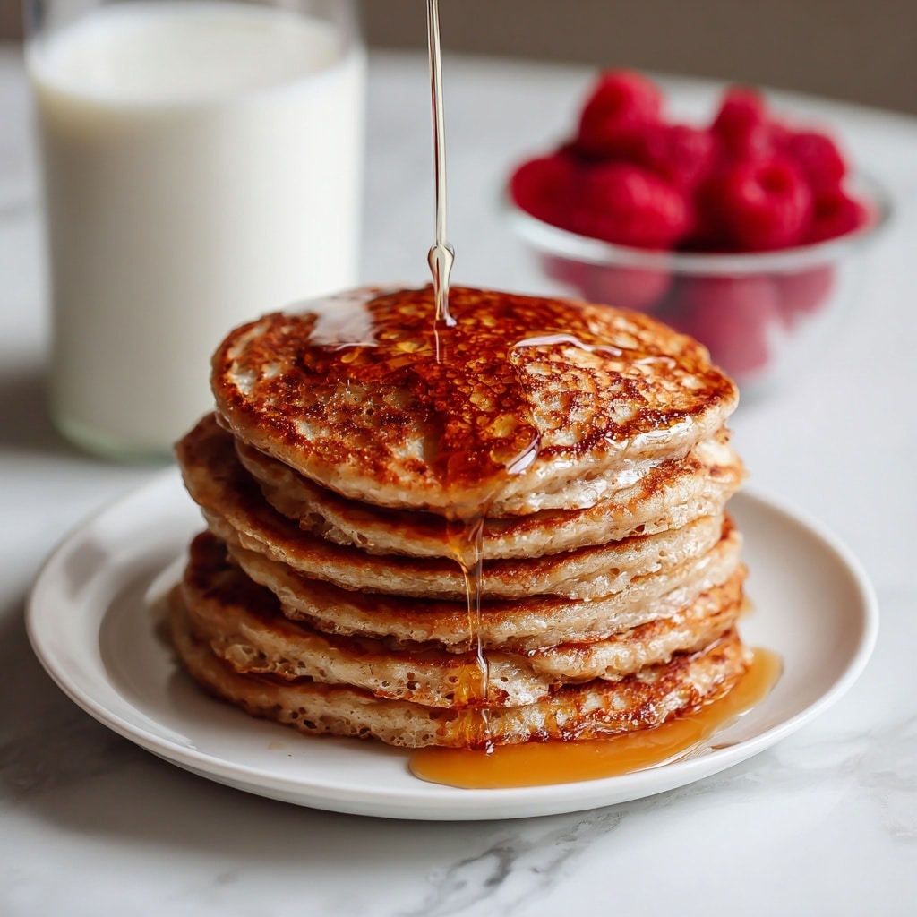 A tall stack of six thick, golden-brown pancakes sits on a white plate against a white marbled background. Each pancake is fluffy with slightly browned edges and soft, light cream interiors visible through small air pockets. The top pancake has a melting square of pale butter slowly spreading across the surface, adding a shiny texture. In the blurry background, there is a glass of milk and some red berries that add a touch of color but remain out of focus. photo taken with an iphone --ar 4:5 --v 7