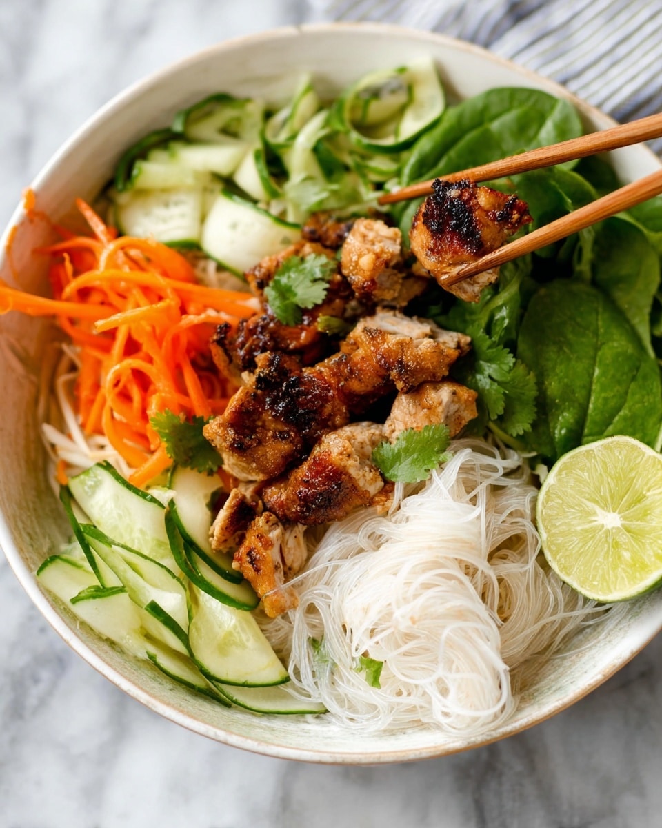 A white bowl filled with a dish showing several layers: at the bottom are thin white rice noodles with a fine texture, topped with grilled brown chicken pieces, some of which are held in a pair of wooden chopsticks by a woman's hand. Around the noodles and chicken, there are fresh green leafy herbs, bright orange carrot sticks, and green cucumber strips arranged in sections. A green lime wedge is placed on one side, adding a fresh touch. The bowl sits on a white marbled surface. photo taken with an iphone --ar 4:5 --v 7