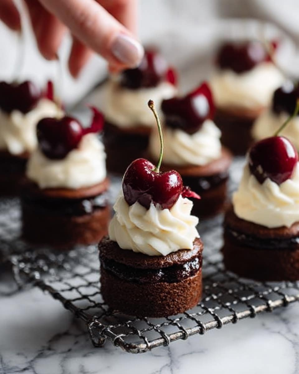 The image shows several small, round chocolate cakes arranged on a silver wire rack. Each cake has three main layers: a dark brown chocolate base, a swirl of white cream on top, and a single dark red cherry with a stem placed in the center of the cream. The cakes have a smooth texture on the chocolate base and a soft, fluffy look to the cream. The background features a white marbled surface. The photo is taken with a woman's hand gently touching one of the cakes. photo taken with an iphone --ar 4:5 --v 7