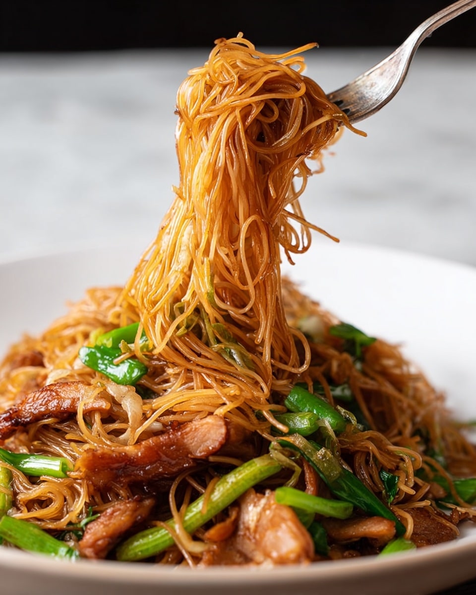 The dish shows thin brown noodles mixed with small pieces of light golden-brown cooked chicken spread evenly throughout. Bright green cut scallions are scattered on top, adding a fresh contrast to the warm colors. There are also fresh green snow peas and thin strips of orange carrot woven through the noodles, creating layers of different textures. The noodles appear glossy and slightly tangled, lightly coated in sauce. The background is a white marbled texture. photo taken with an iphone --ar 4:5 --v 7