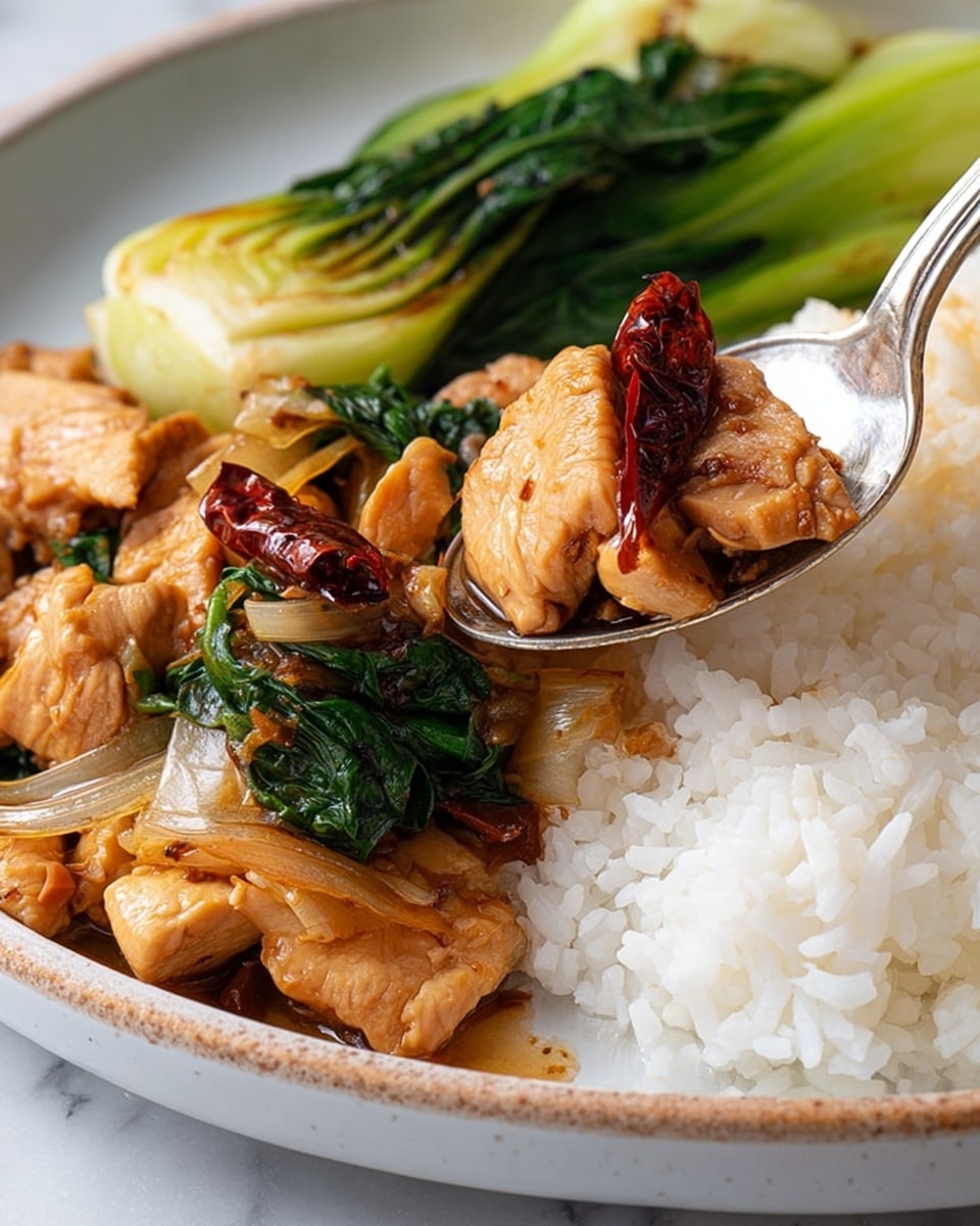 The image shows a close-up view of a plate with three layers of food. The first layer is white rice, fluffy and slightly sticky, positioned on the right side of the plate. The second layer consists of cooked chicken pieces with a shiny, light brown sauce coating them, scattered over and beside the rice. The third layer includes bright green bok choy with a soft texture, placed on the left side of the plate alongside the chicken. A piece of dried red chili rests on top of one chicken chunk on a silver spoon, which lifts some rice mixed with sauce and chicken near the plate's edge. The plate is white with a slightly speckled rim, set on a white marbled texture background. photo taken with an iphone --ar 4:5 --v 7