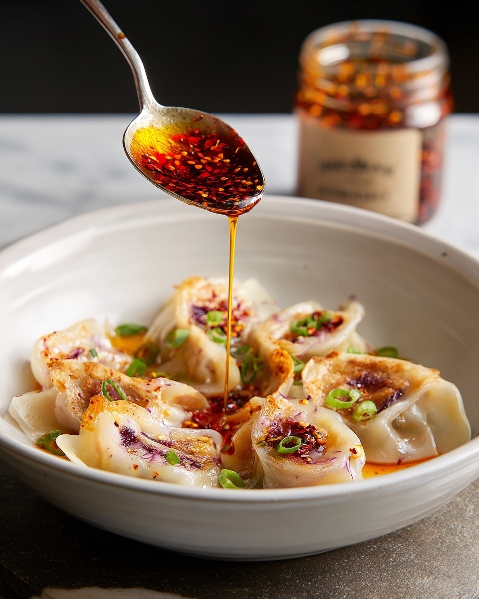 A white bowl holds six translucent dumplings with slightly browned spots scattered on the surface; inside, shades of purple and orange show through the thin dough, indicating colorful fillings. Small green onion slices are sprinkled around and on top of the dumplings. Above, a silver spoon drips bright red chili oil onto the center dumpling, glistening as it falls. In the background, a jar of chili oil and its white lid sit on a dark textured surface, contrasting with the white marbled texture under the bowl. photo taken with an iphone --ar 4:5 --v 7