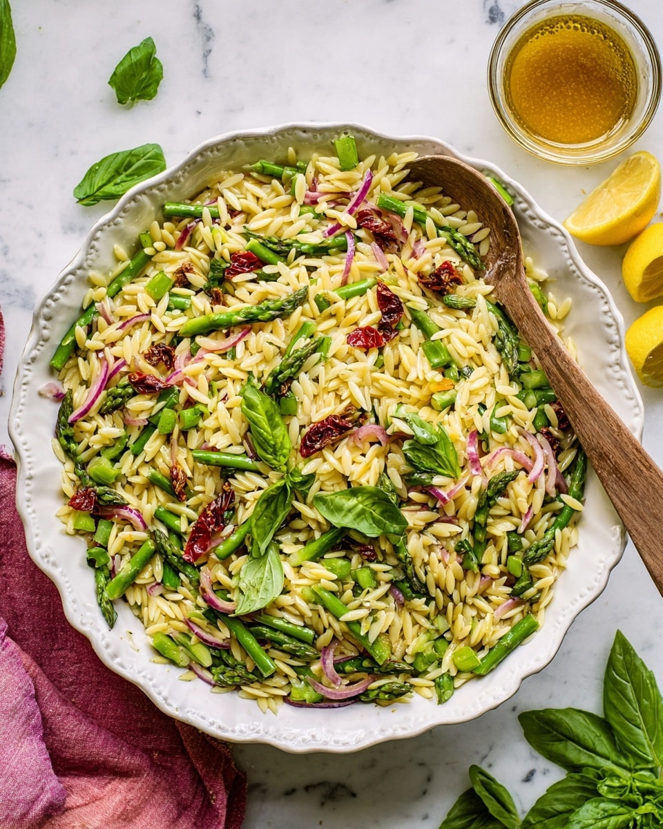 The image shows a white plate with a colorful orzo salad made of three main layers: the bottom layer is yellowish orzo pasta, soft and slightly oily; the middle layer has bright green asparagus cut into pieces and snap peas, mixed with thin slices of light purple-red onion and chunks of deep red sun-dried tomatoes; the top layer is bright green fresh basil leaves scattered over the salad. A wooden spoon rests inside the plate, partially covering the salad. The background is a white marbled surface, and a pink cloth is partly visible on the bottom left side. Photo taken with an iphone --ar 4:5 --v 7