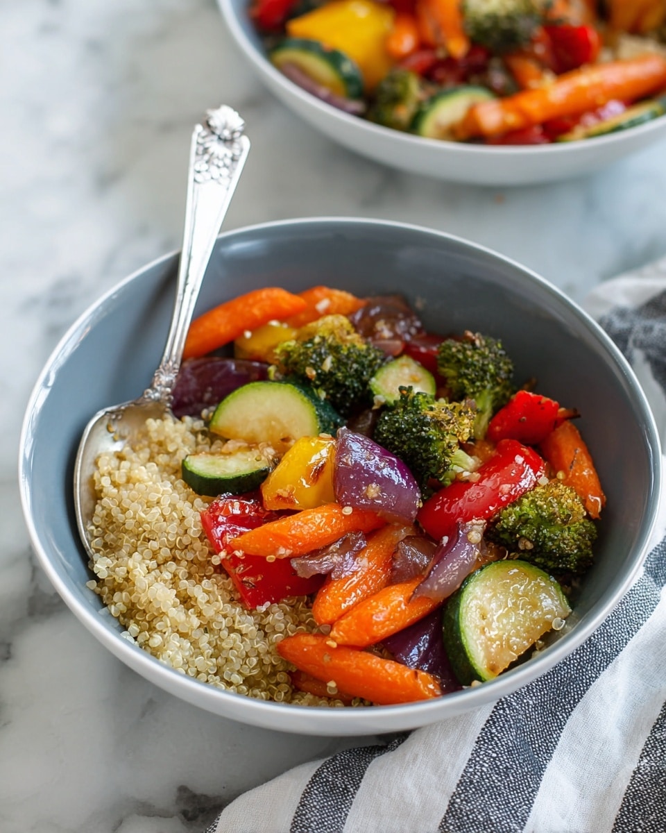 A bowl filled with two layers: the bottom layer is light beige quinoa with a soft, grainy texture, and the top layer is a mix of colorful roasted vegetables including bright orange carrot slices, green broccoli florets, dark red cherry tomatoes, rings of green zucchini, red bell pepper pieces, yellow bell pepper chunks, and purple red onion pieces. A silver spoon with decorative handle rests inside the bowl, which is white. The setting is a white marbled surface, and a striped cloth is partially visible on the right side. In the blurred background, another similar bowl with the same dish can be seen. Photo taken with an iphone --ar 4:5 --v 7