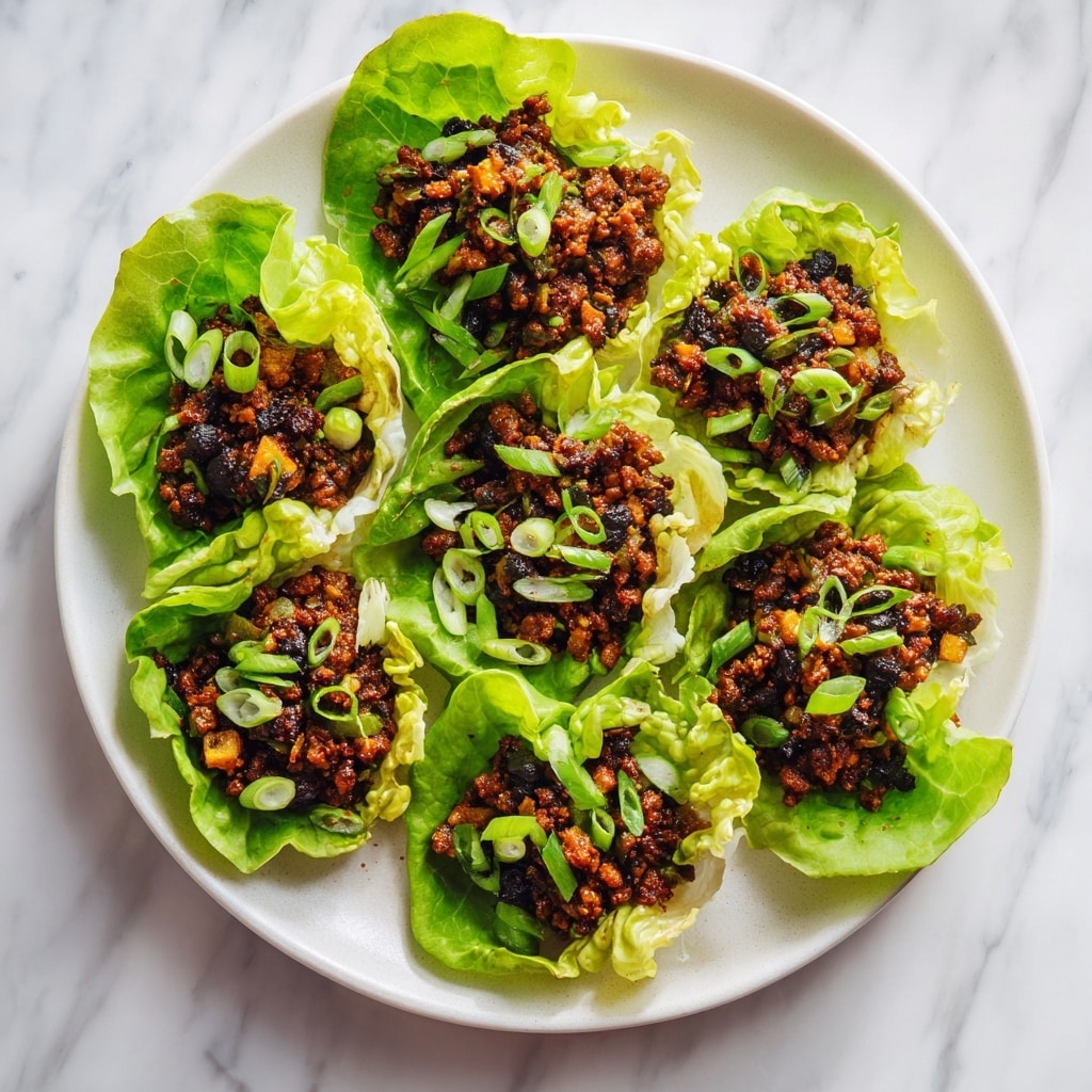 The image shows five lettuce wraps arranged on a large white plate, placed on a white marbled surface. Each wrap has two main layers: a bright green, soft lettuce leaf on the bottom with a rough textured ground meat mixture on top. The meat is brown with bits of dark sauce and some sliced green chili peppers scattered throughout. One wrap is being held by a woman's hand, with fingers gently lifting the edges of the lettuce to hold the filling inside. Photo taken with an iphone --ar 4:5 --v 7