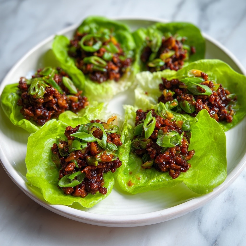 A white plate holds eight bright green lettuce cups, each filled with a dark brown mixture of cooked minced meat and vegetables. The mixture has a slightly chunky texture and is topped with thin slices of green onion, adding a fresh contrast. The lettuce leaves are large, crisp, and slightly curled at the edges, creating a natural bowl shape for the filling. The plate sits on a white marbled surface visible around its edges. photo taken with an iphone --ar 4:5 --v 7