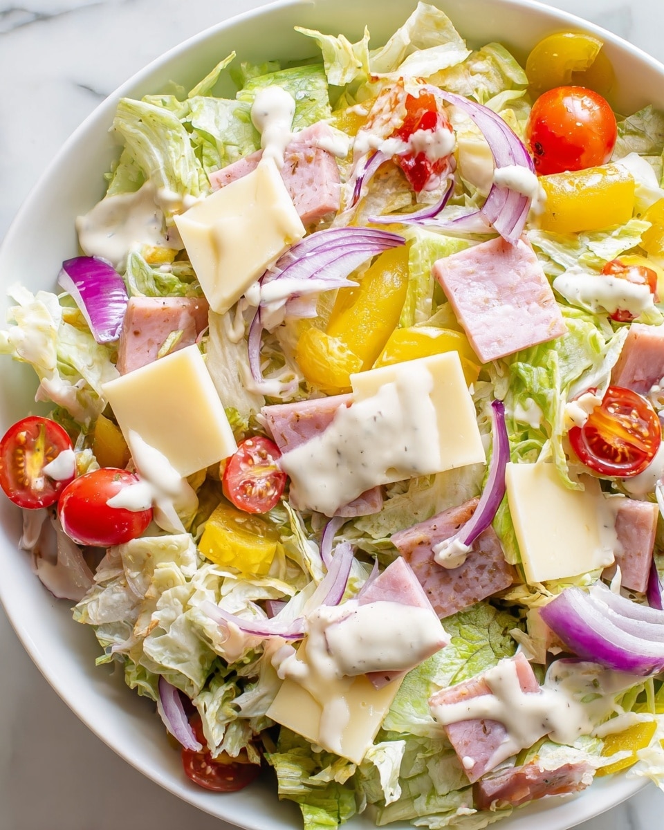 A white round plate holds a fresh salad with thin layers of shredded light green lettuce forming the base. Scattered throughout are small, bright red cherry tomato halves, thin strips of light purple onion, and light yellow cheese squares. There are also pieces of pale pink deli meat mixed in. The salad is lightly coated with a creamy, white dressing drizzled unevenly over the top. Two shiny gold forks rest on the right side of the plate, placed on a white marbled surface. photo taken with an iphone --ar 4:5 --v 7