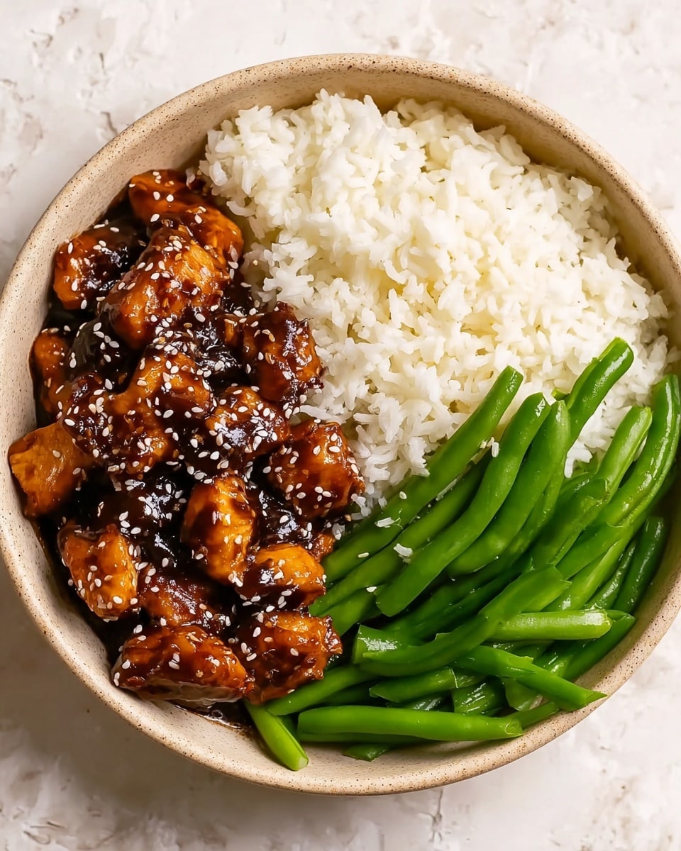 A beige bowl holds a three-part meal arranged side by side on a white marbled texture. On the left side, there are shiny, golden-brown chunks of chicken covered in a glossy dark brown sauce, sprinkled with white sesame seeds. The middle section features fluffy, white steamed rice with a soft texture. On the right, there are slender green beans that look vibrant and slightly glossy, resting beside the rice. The overall presentation is neat with clear division between each part of the dish. photo taken with an iphone --ar 4:5 --v 7