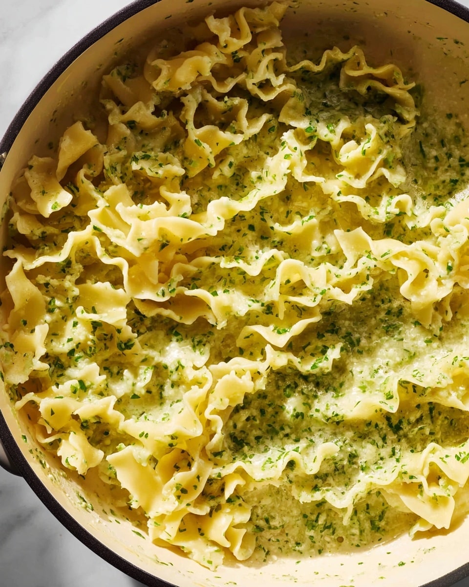 A close-up view shows creamy pasta with three layers to the noodles; the first layer is light yellow with curly, ruffled edges, the second layer has a white creamy sauce with small green herb bits spread evenly, and the third layer is a mix of smooth and slightly textured pasta strands, all lifted from a white bowl by a fork held by a woman's hand. The background has soft, blurred darker tones, while the bowl is set on a white marbled surface. photo taken with an iphone --ar 4:5 --v 7